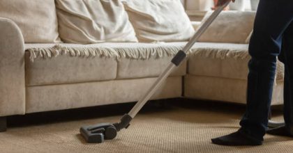 Close up cropped image young african american guy using vacuum cleaner, cleaning whitish carpet, removing dust in modern living room, daywork routine, housekeeping, home routine concept.