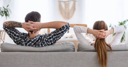 Joint rest at home after cleaning. Guy and girl relaxing on couch with hands clasped behind head.