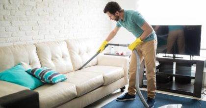 Handsome Hispanic man using a vacuum cleaner to take away the dust in the couch